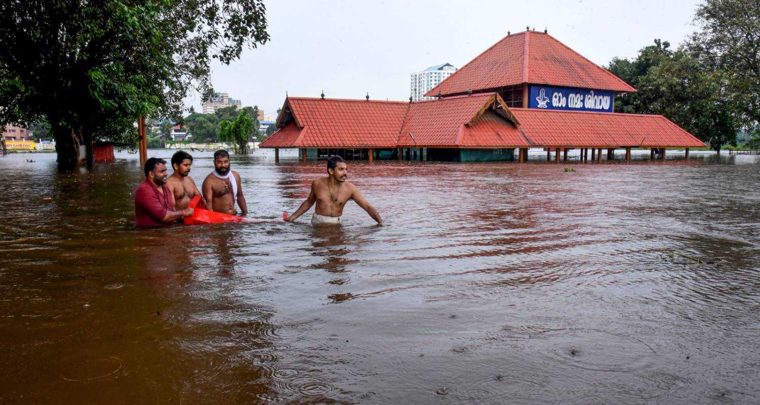 Kochi: People make their way through a flooded area near the Aluva Mahadeva Temple which got partially submerged due to rising water levels of the Periyar river following heavy rains, in Kochi district, Tuesday.