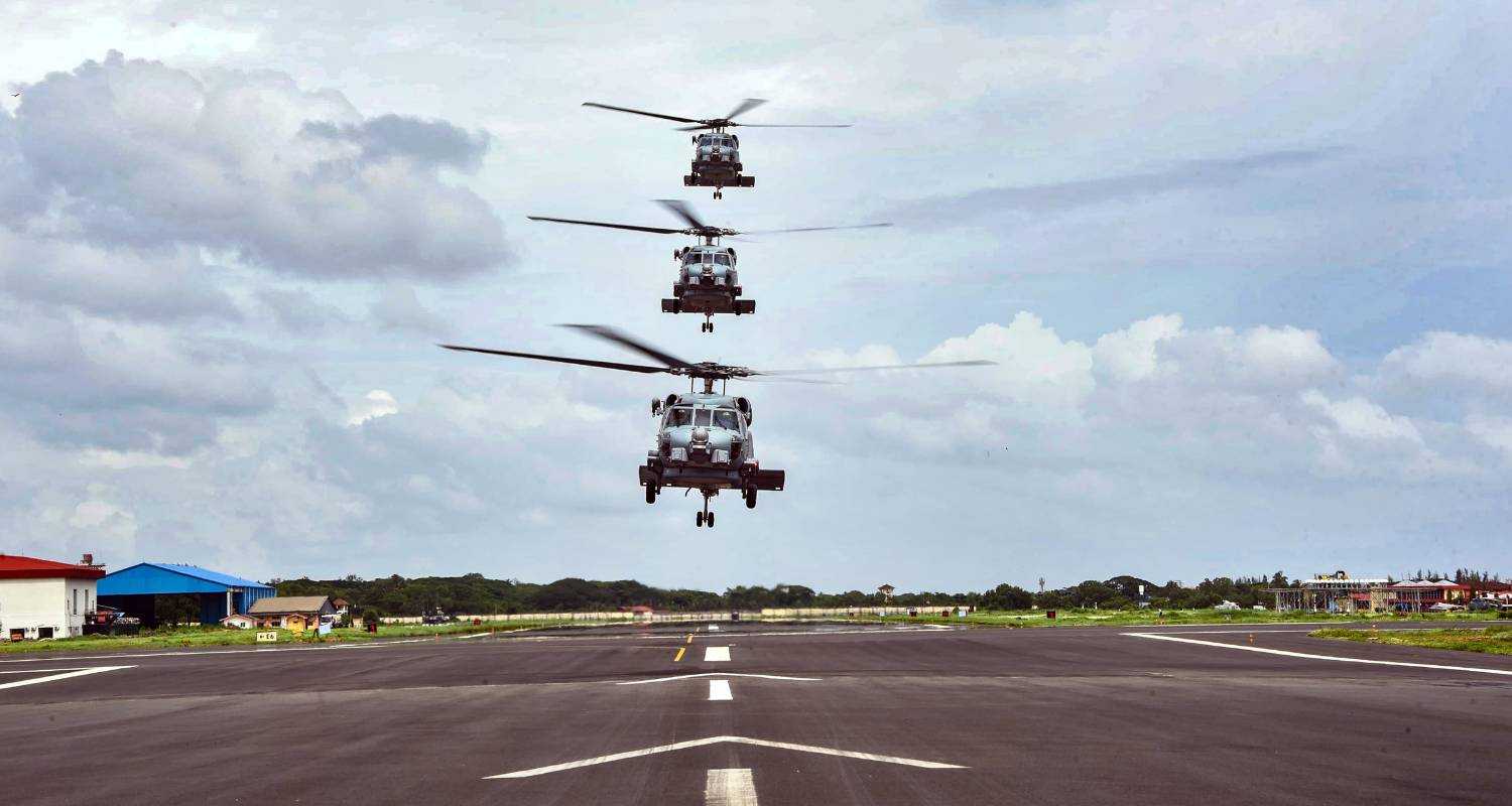 Three MH-60R Seahawk helicopters in a vertical formation above the runway at INS Garuda, signifying their imminent induction into the Indian Navy's air squadron.