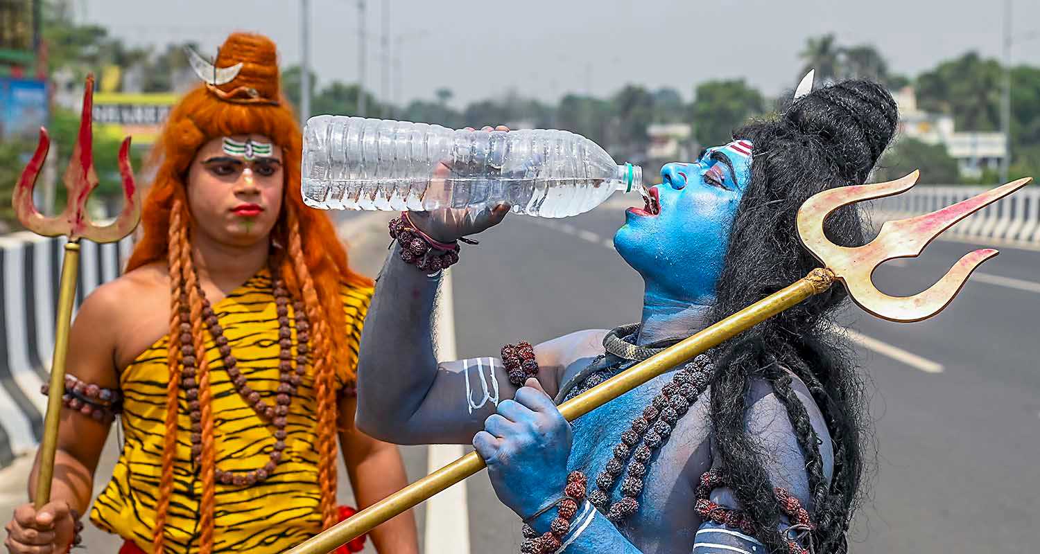 An artist dressed as Lord Shiva drinks water on a hot summer afternoon, in Nadia district