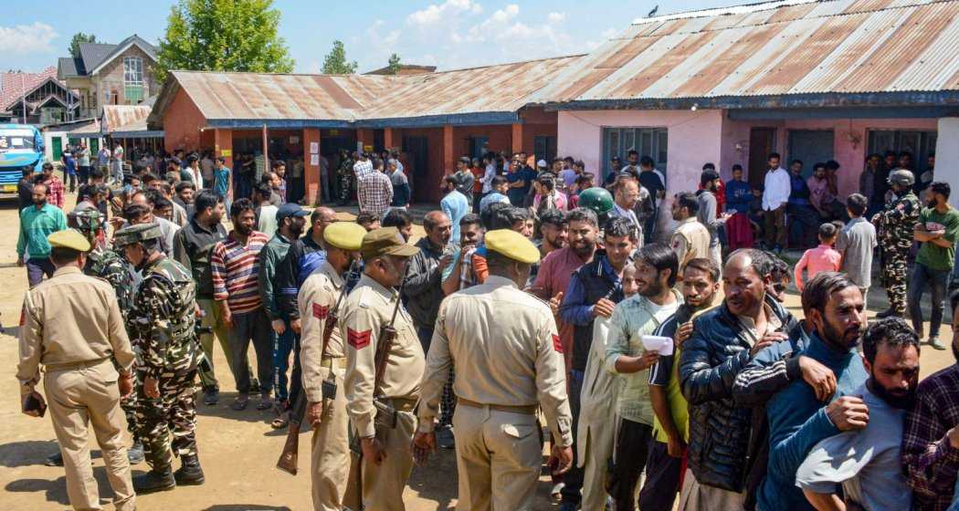 Security personnel stand guard as voters wait in long queues at a polling booth during the 5th phase of elections, in Baramulla district of north Kashmir, Monday, May 20, 2024.