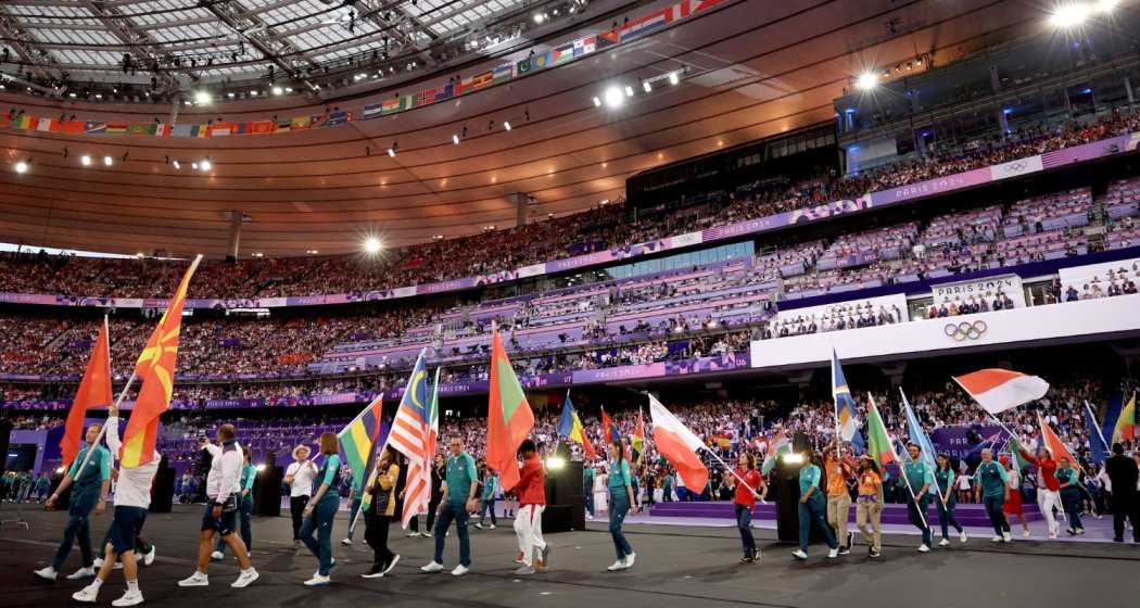 Athletes gather in the Stade de France during the closing ceremony, celebrating the conclusion of the Paris Olympics with flags, camaraderie, and a festive atmosphere.