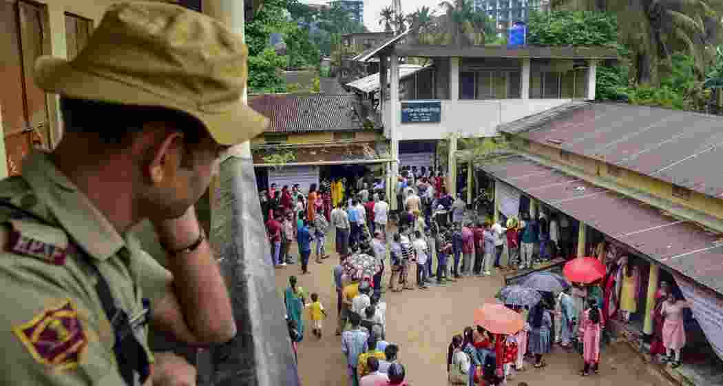 A security personnel stands guard as voters wait in a queue to cast their votes at a polling station for the third phase of Lok Sabha polls in Guwahati on Tuesday.