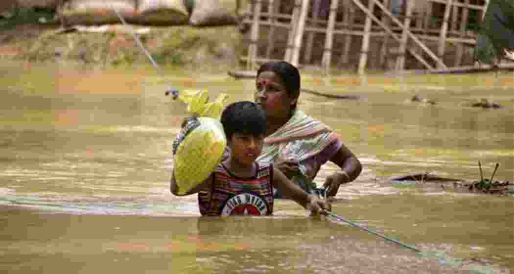 A woman and her child try to walk through a flooded road following rains after the landfall of cyclone Remal, in Nagaon district of Assam on Saturday, June 1, 2024.