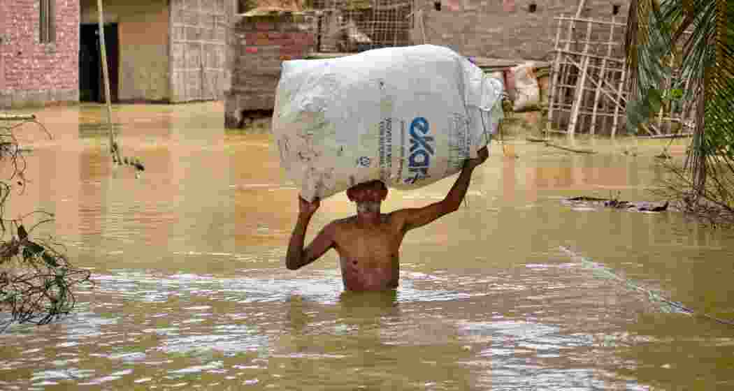 A man carries his belongings as he walks through a flooded road following rains after the landfall of cyclone 'Remal', in Nagaon district of Assam on Saturday.