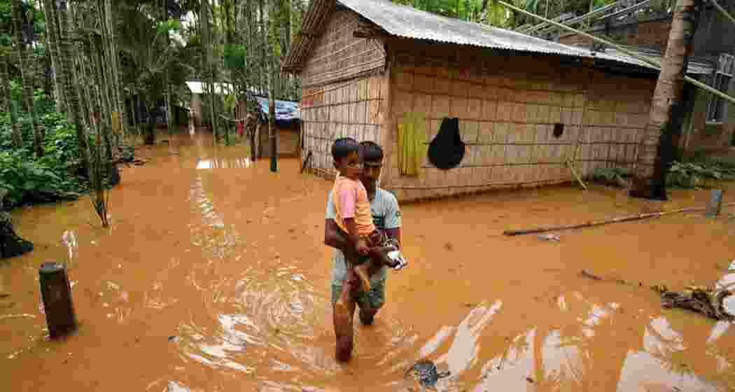 A man carries a child in a flooded village after heavy rains following the landfall of Cyclone Remal at Singi Mari near Kampur in Nagaon district of Assam.