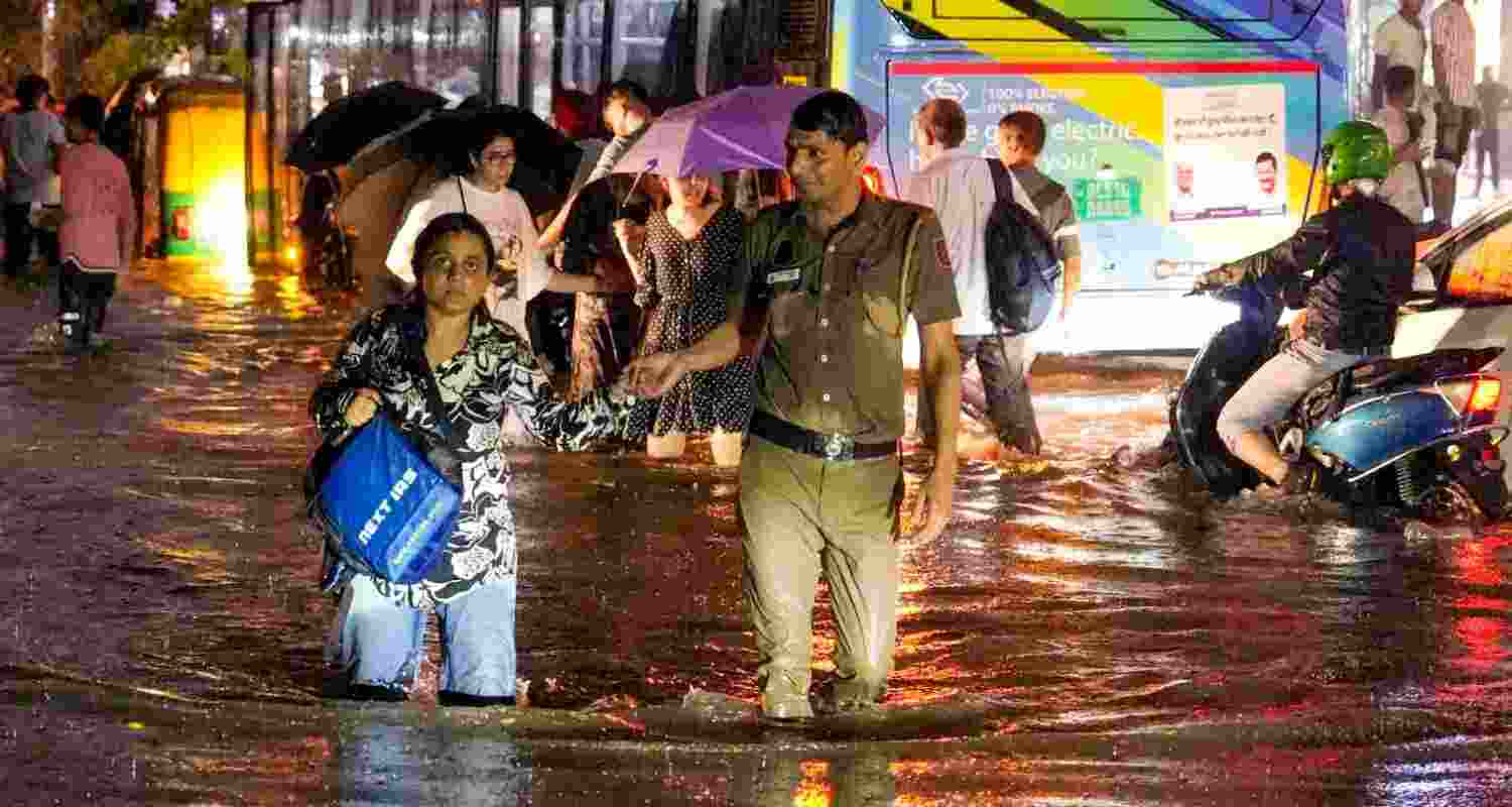 A woman being assisted by a police official while wading through a waterlogged road during rain near Pusa Road area, in New Delhi, Wednesday. 