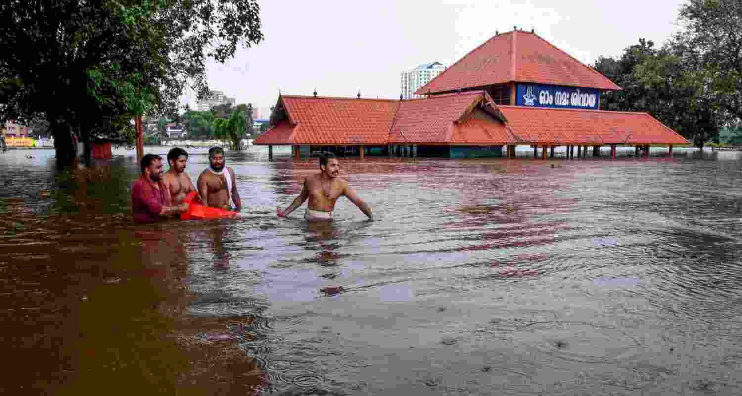 Kochi: People make their way through a flooded area near the Aluva Mahadeva Temple which got partially submerged due to rising water levels of the Periyar river following heavy rains, in Kochi district, Tuesday.