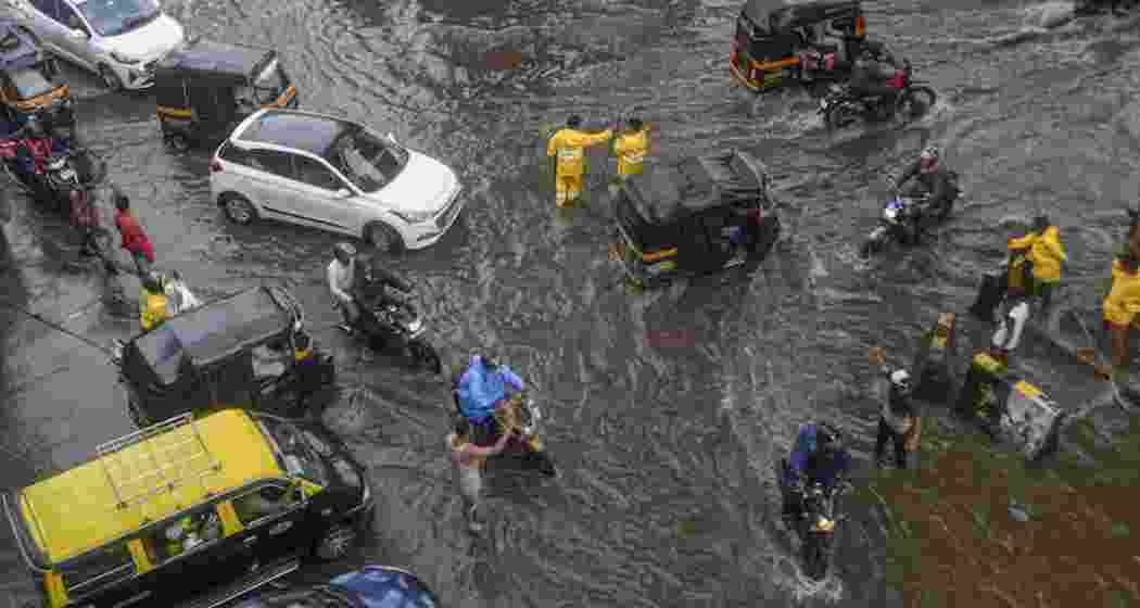 Commuters wade through a waterlogged street following rains, In Mumbai.