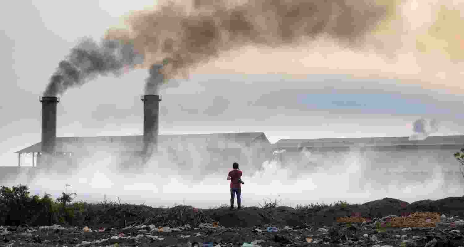 A man stands next to a factory releasing toxic gases.