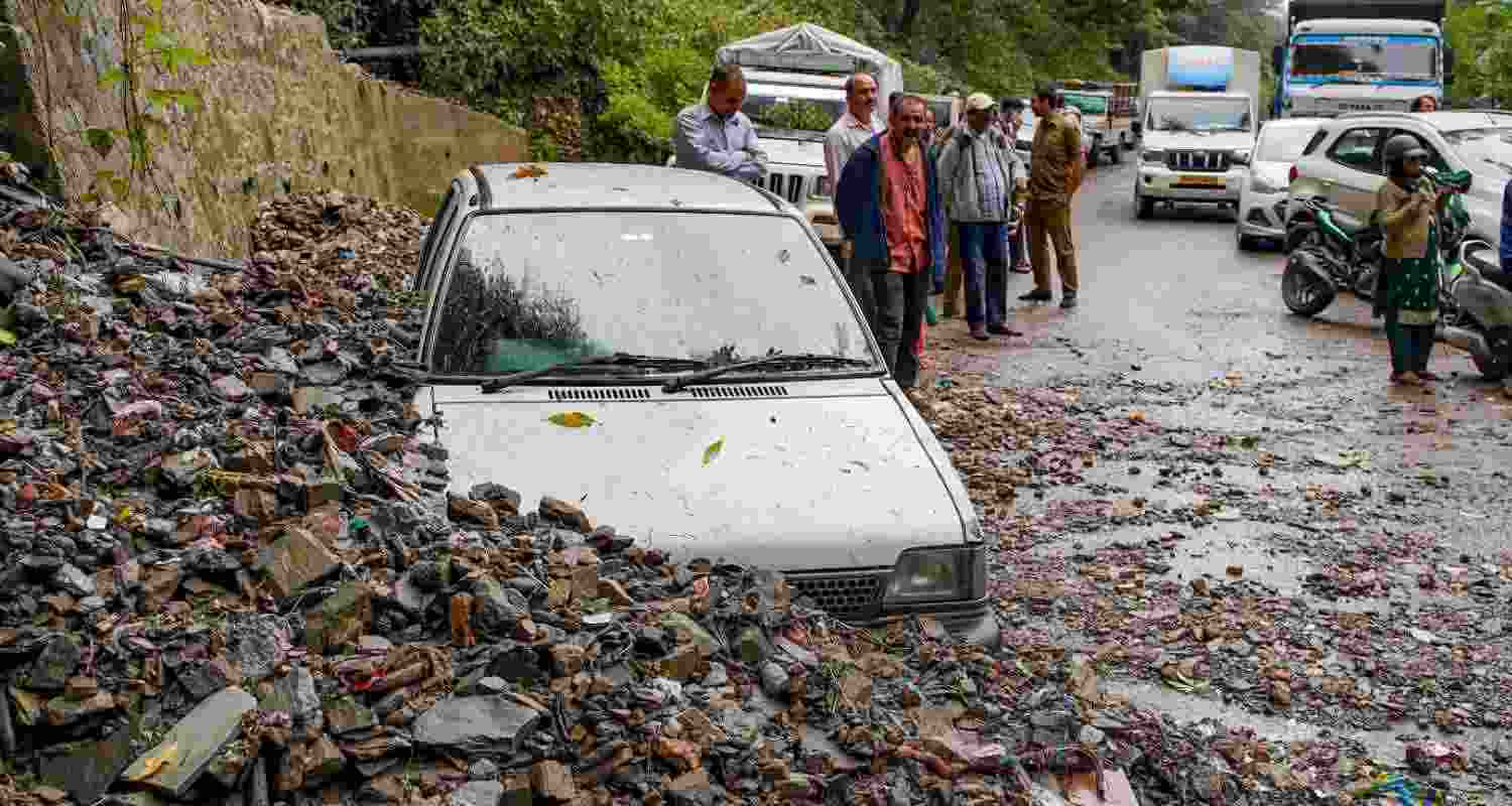 Workers clear a road that was blocked by an uprooted tree following heavy rainfall, in Shimla, Thursday. 