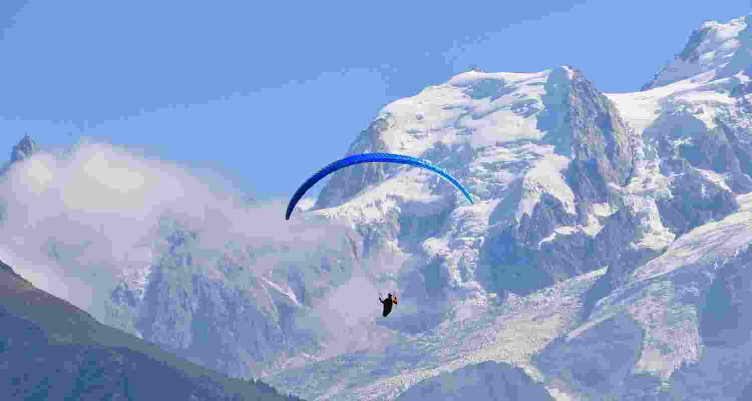 A paraglider in the air against snow capped mountains.