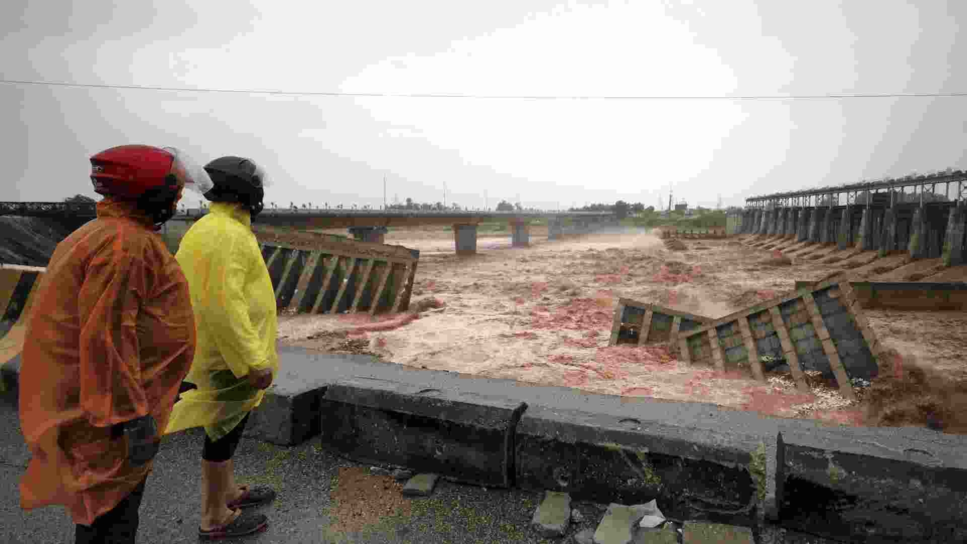 People protect themselves with raincoats while looking at the damaged remains of the 4th Tawi Bridge, after rain continues to lash parts of the city, in Jammu, Wednesday.