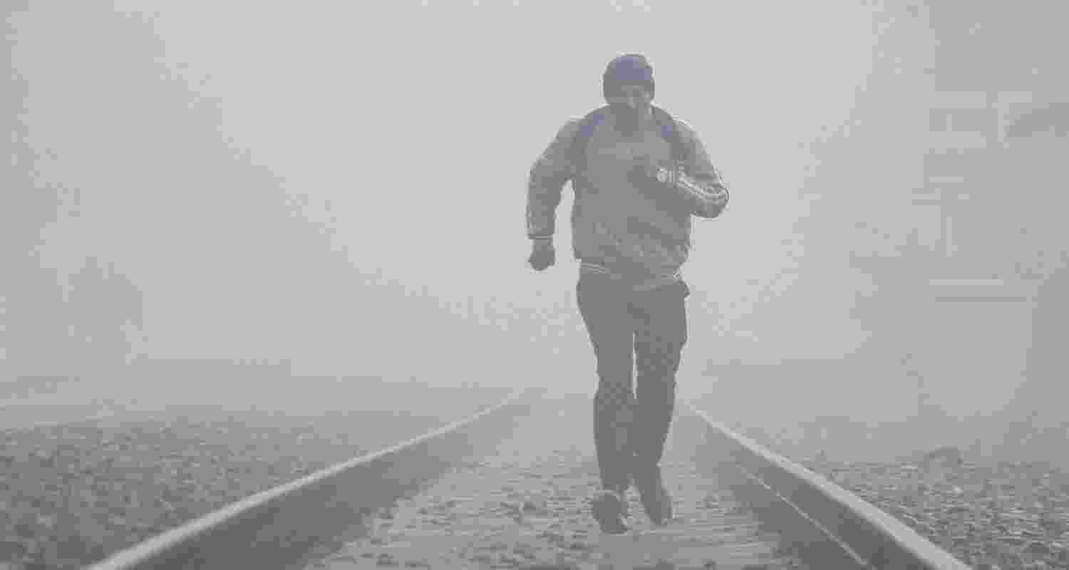 A man runs on a railway track amid low visibility on a winter morning near Basai Dhankot Railway station, in Gurugram