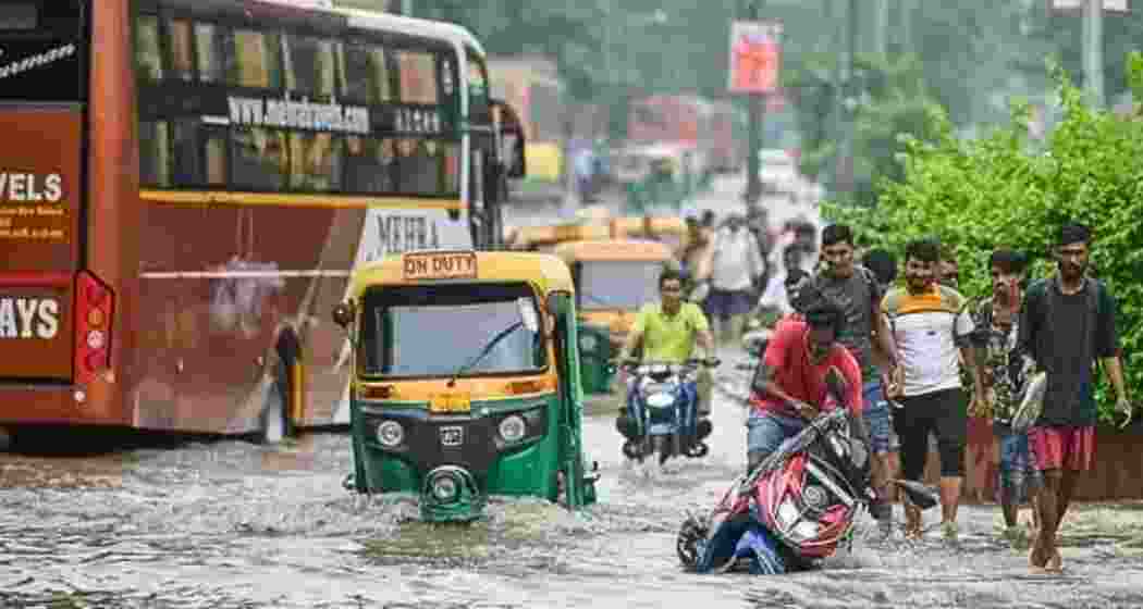 Commuters wade through waterlogged streets in Delhi after heavy overnight rain and thunderstorms on Sunday paralysed traffic and disrupted over 100 flights at the Indira Gandhi International Airport.
