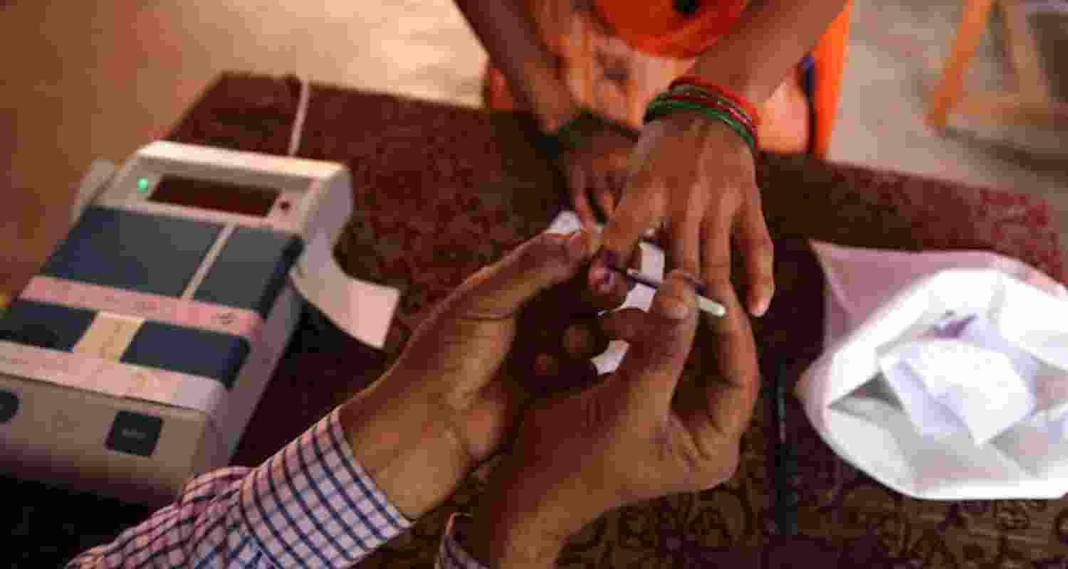 An election booth worker applies indelible to a voter's finger.