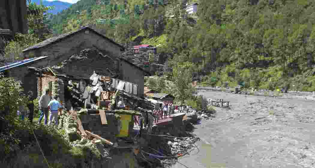 People gather near a house after it was partially washed in the Beas river flowing in spate due to heavy rainfall, in Kullu district, Himachal Pradesh on Wednesday.