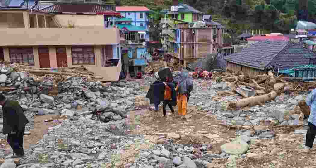 Locals carry their belongings as they walk amid the debris at a flood-affected area, at Thunag in Mandi district, Monday, July 7, 2025. Since the onset of monsoon, Himachal Pradesh has reported 78 deaths, of which 50 were linked to rain-related incidents such as cloudbursts, flash floods and landslides. (PTI Photo)