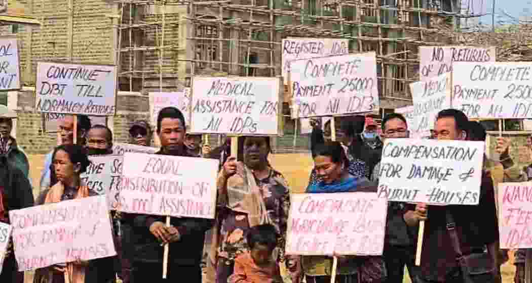 Internally displaced persons from Kangpokpi district hold placards at Keithelmanbi Military Colony, demanding justice, full compensation and rehabilitation before returning home amid ongoing government rehabilitation plans.