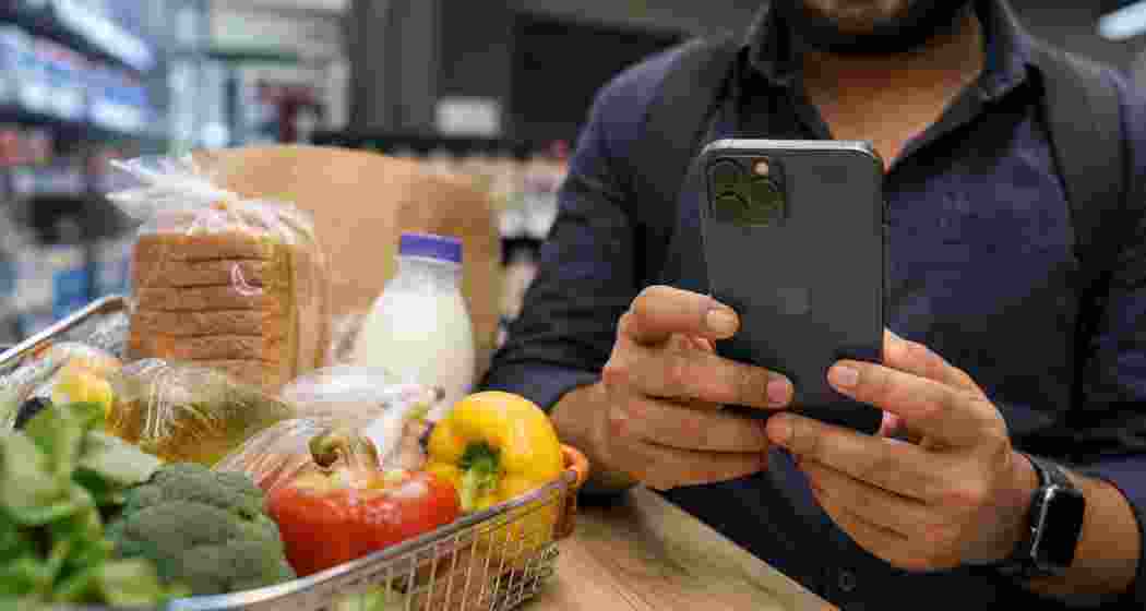 A customer uses a premium smartphone while shopping for groceries, symbolising India’s shift in consumer spending from essentials to digital services, gadgets and lifestyle experiences. (Representational Image)
