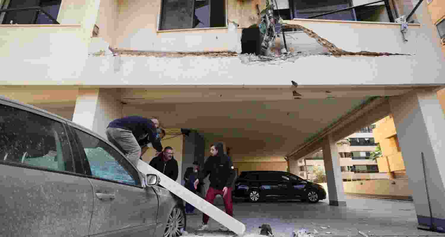 People remove debris from a damaged car at a site where a projectile carrying leaflets hit an apartment building in Beirut, Lebanon, Saturday, March 28, 2026. 