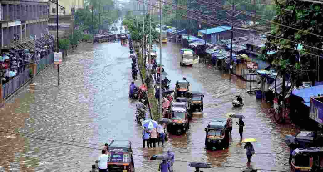 Commuters make way through a waterlogged road amid rainfall, in Palghar, Maharashtra.