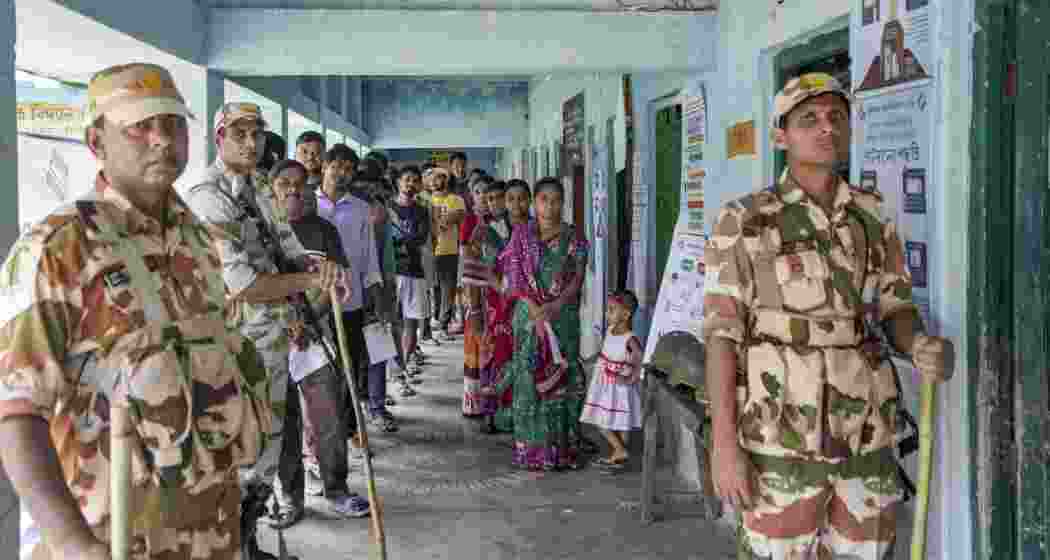 Security personnel stand guard as voters wait in a queue to cast their votes at a polling station during a repoll ordered by the Election Commission following reports of electoral malpractices, at Magrahat Paschim constituency, in South 24 Parganas district, West Bengal on Saturday.