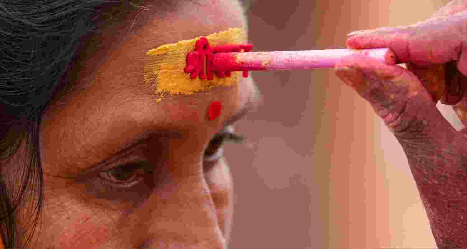 A devotee adorns a holy 'tilak', being highlighted with vermilion, highlighting an embossed impression of 'Shree Ram', ahead of the Pran-Pratishtha ceremony in Ayodhya. The Pran Pratishtha ceremony is set to begin at 12:20 PM IST. Nearly 8000 guests are expected to attend, which include dignitaries, politicians, actors, sportspersons and social workers.