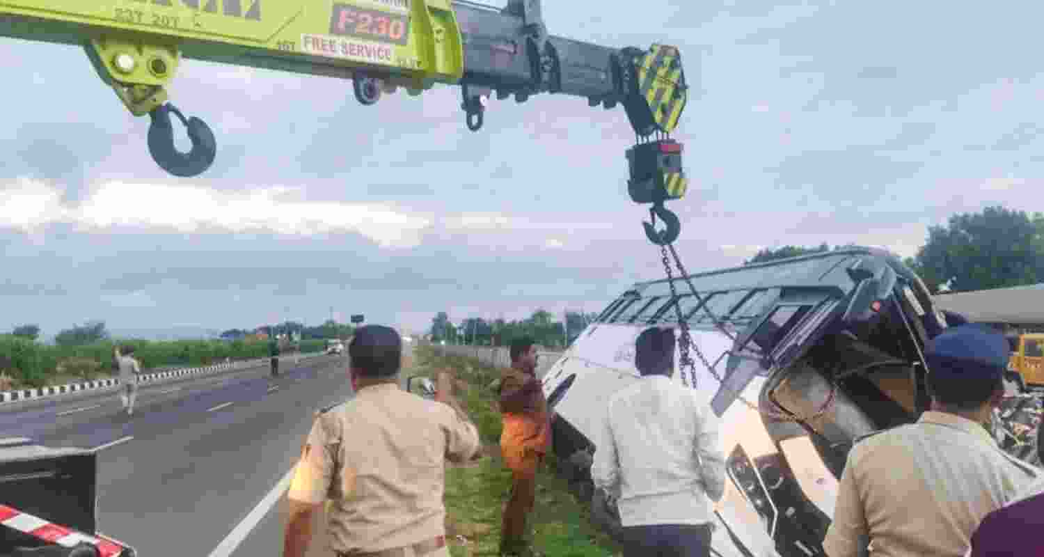 A recovery vehicle lifting the overturned private bus as people gather at the accident site near Aimangala in Chitradurga district of Karnataka on Friday.