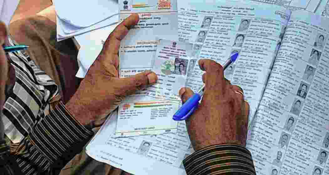An election official checks an Aadhaar and voter card. An election official checks an Aadhaar and voter card.